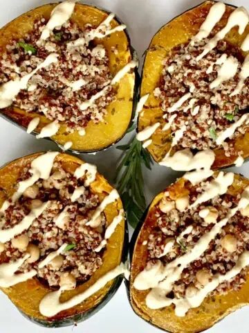 Quinoa stuffed acorn squash served up on a white plate with cashew drizzle.