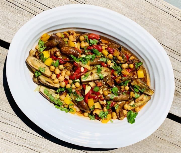 Fairy Tale Eggplant Sauté - a colorful mix of eggplant, red peppers, chick peas and spices cooked and displayed on a white serving platter with a wood background