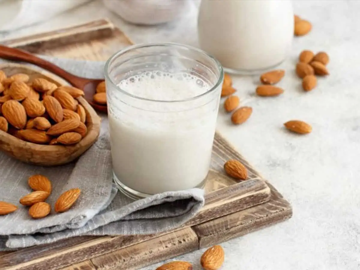 A glass of almond milk with almonds on a table.
