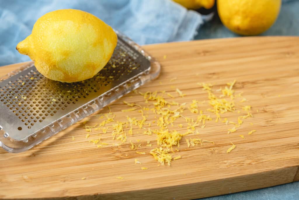 Microplane with fresh lemon making lemon zest on wooden board against a blue background