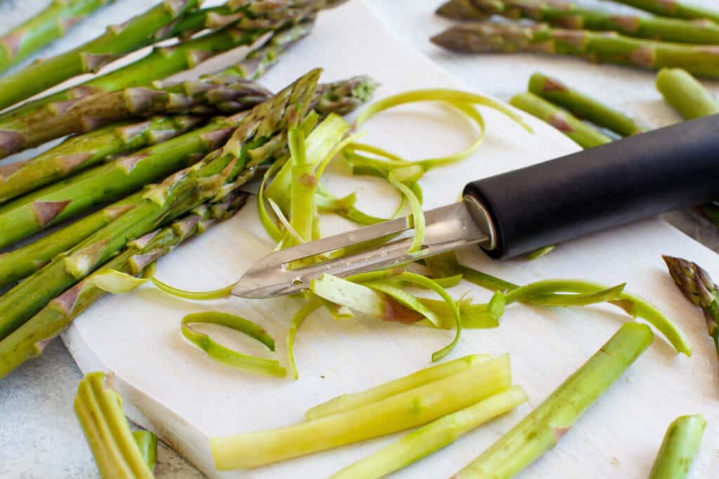 Cutting fresh asparagus with a peeler on a white table close up