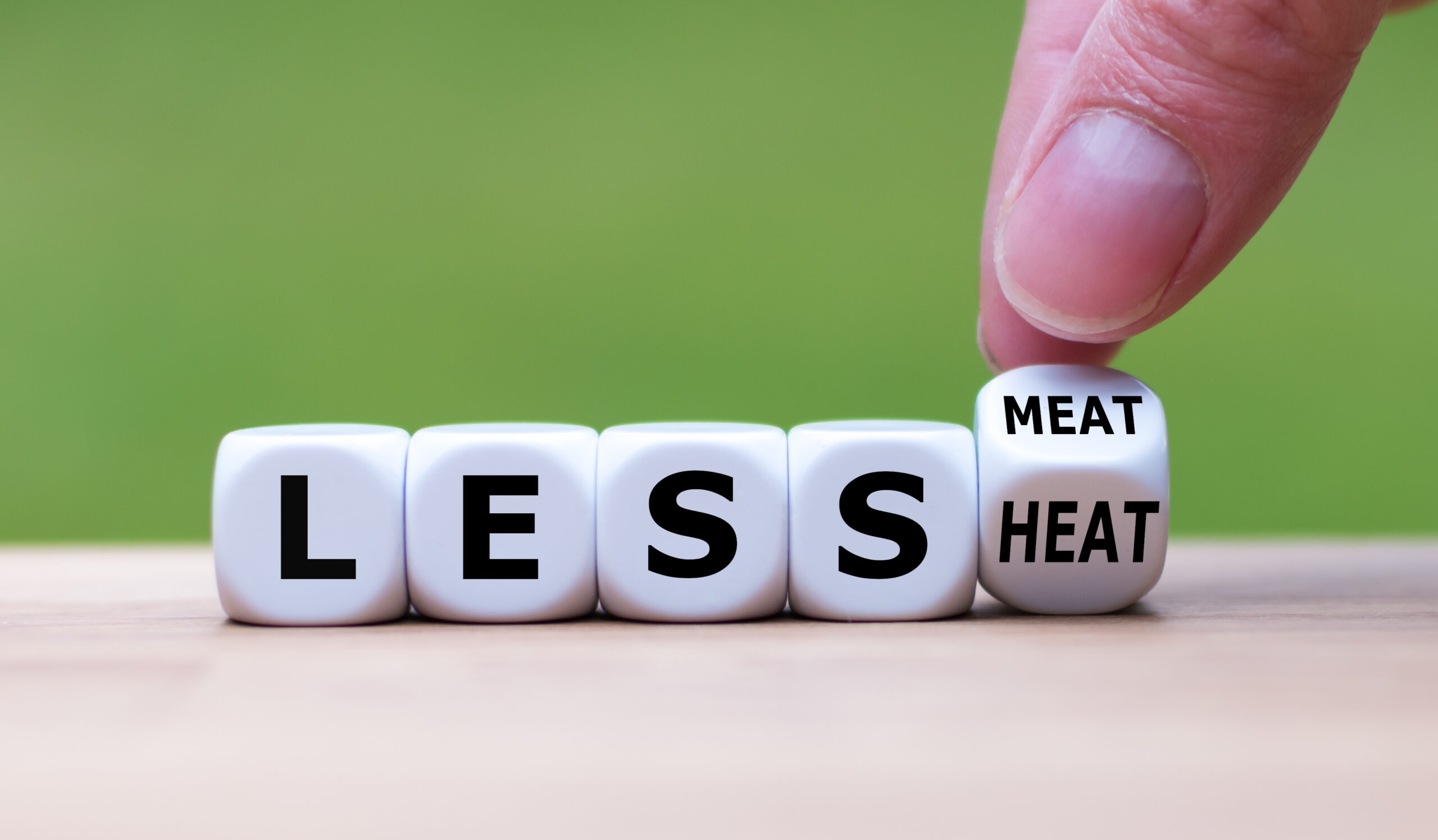 Symbol for eating less meat to save the planet. Hand turns a dice and changes the expression "less meat" to "less heat".