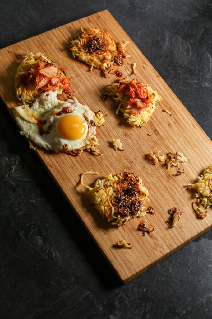 Crispy kohlrabi hash browns cooked and placed on a wooden cutting board with toppings