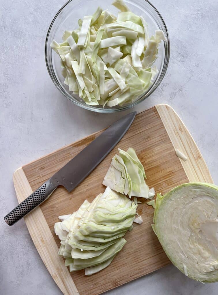 Cabbage on cutting board with knife, sliced pieces in glass bowl
