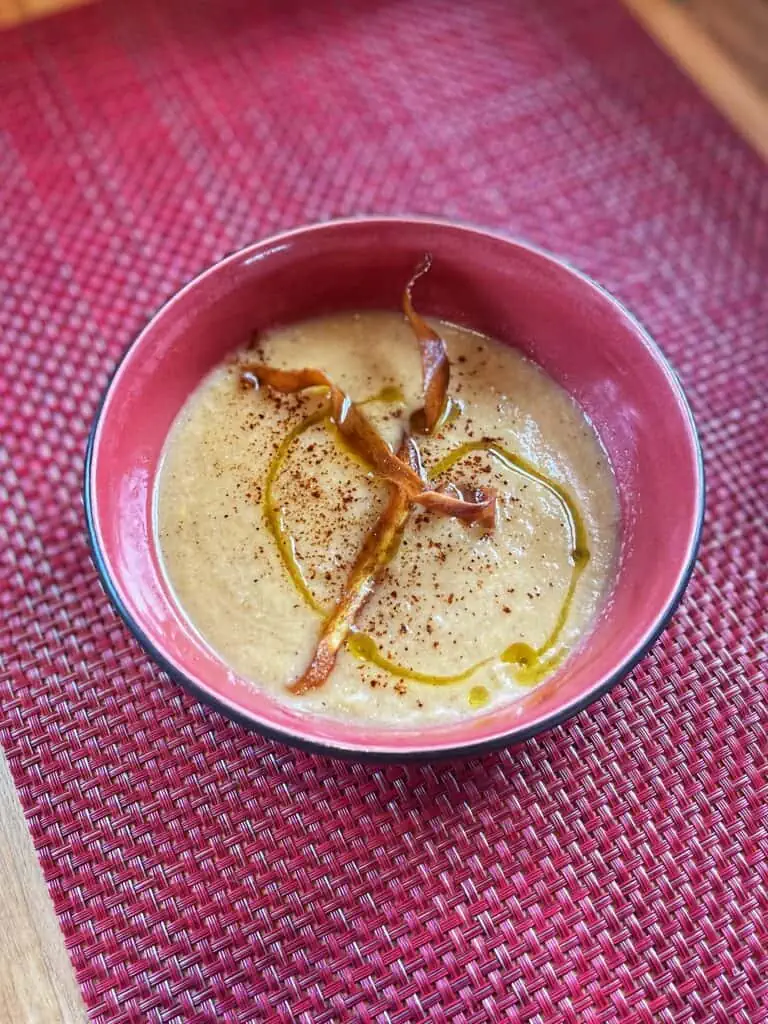 Roasted Parsnip & Cauliflower Soup with Parsnip Ribbons and a drizzle of oil in a pink bowl