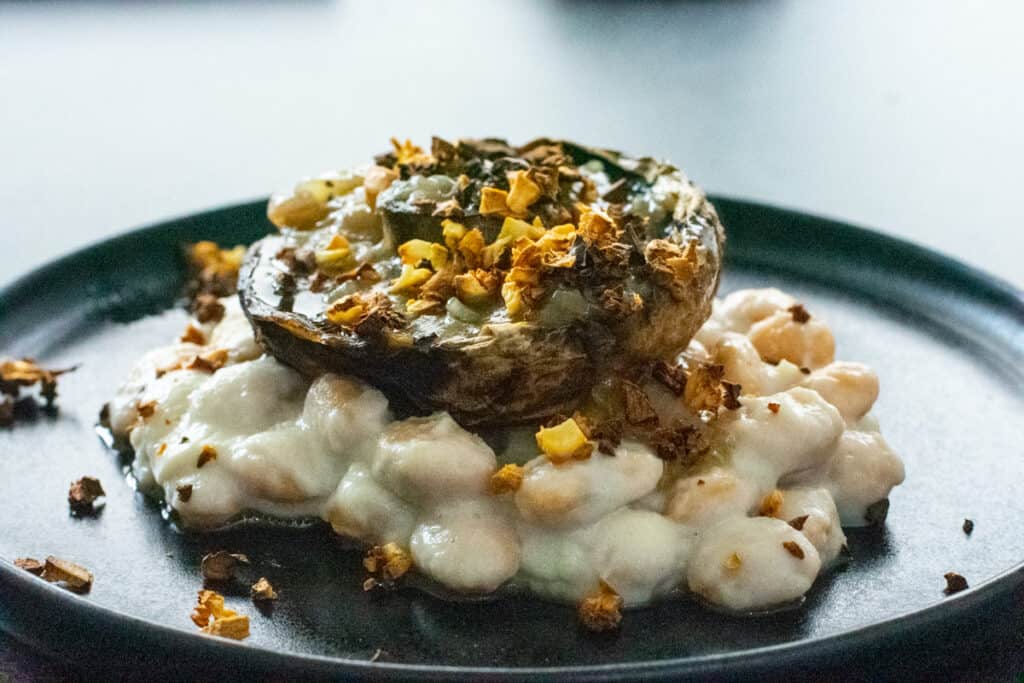 Jerusalem artichoke. butter bean, mushroom and whiskey sauce on a dark plate