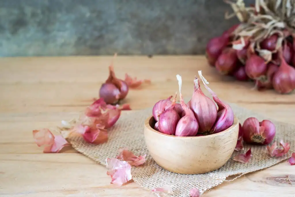 shallots in bowl on old wooden table with old wallpaper and shallots bunch background