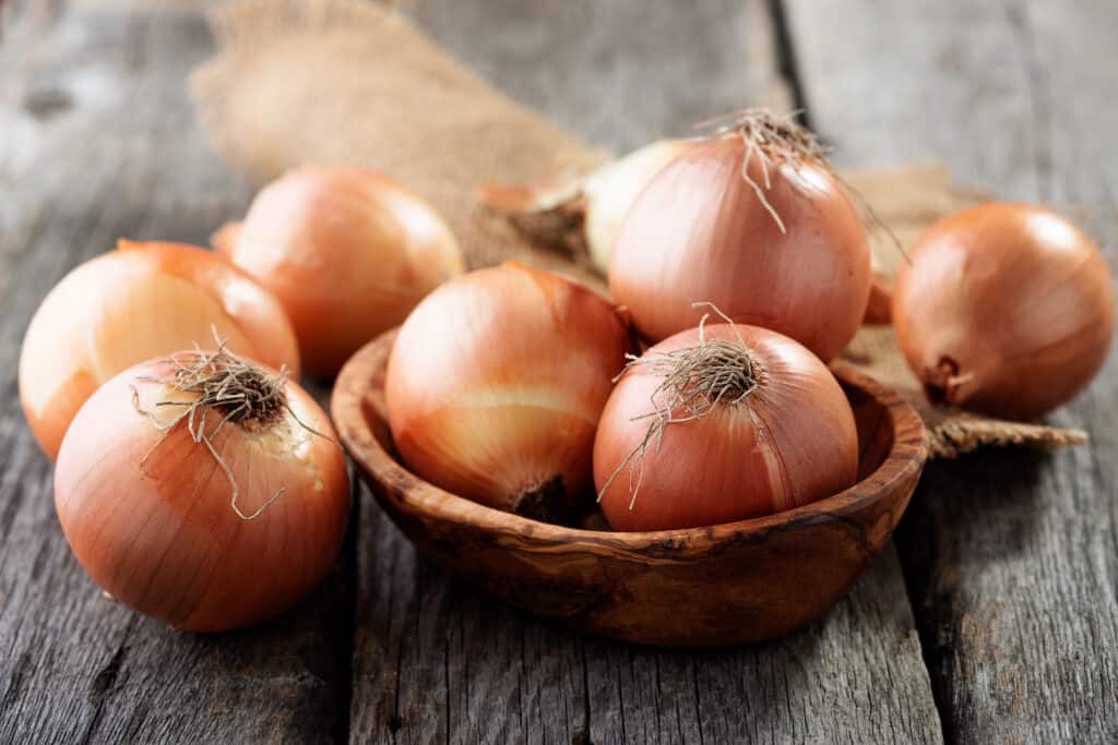 whole sweet onions in a wooden bowl on a dark table