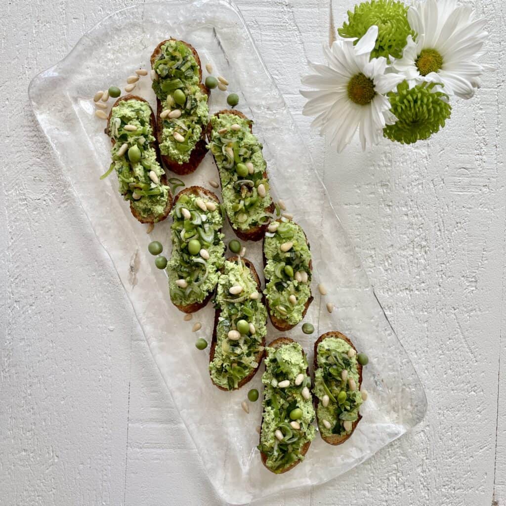 Sweet Pea Crostini on a glass platter next to a vase of flowers