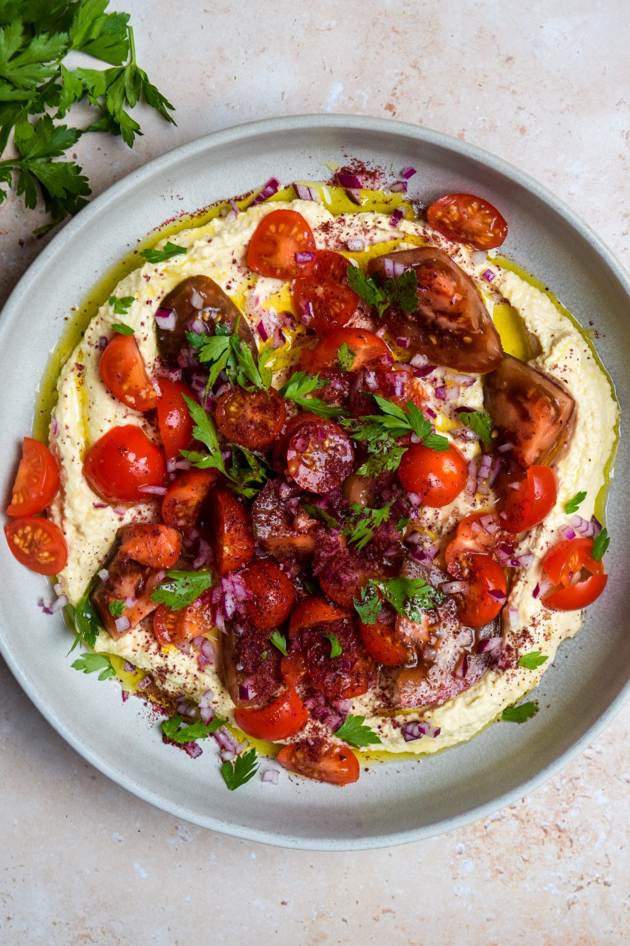 Plate of hummus topped with parsley and tomatoes.