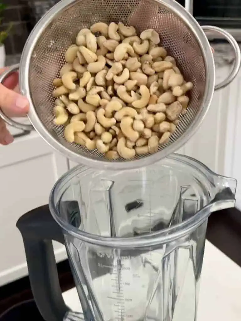 Nuts in a metal strainer being placed in a blender.