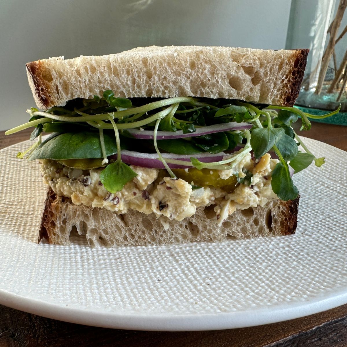 Vegan tuna salad sandwich on a plate with greens and wheat bread.