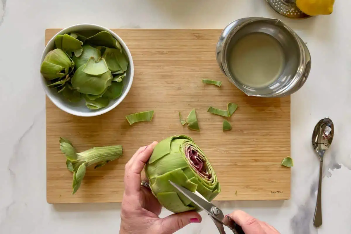 Trimming off the leaves on the cut artichoke.