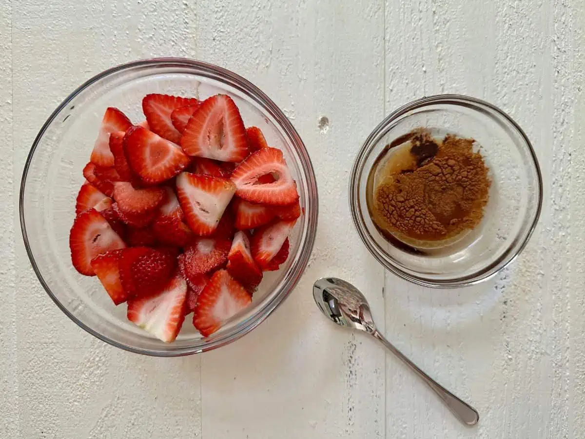 Strawberries in a bowl with a bowl of sugar and liquid ingredients next to it.