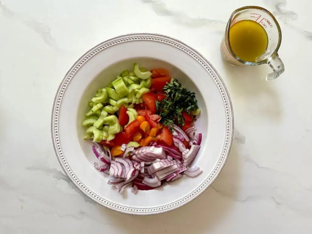 Vegetables in a bowl with the dressing in a measuring cup off to the side.