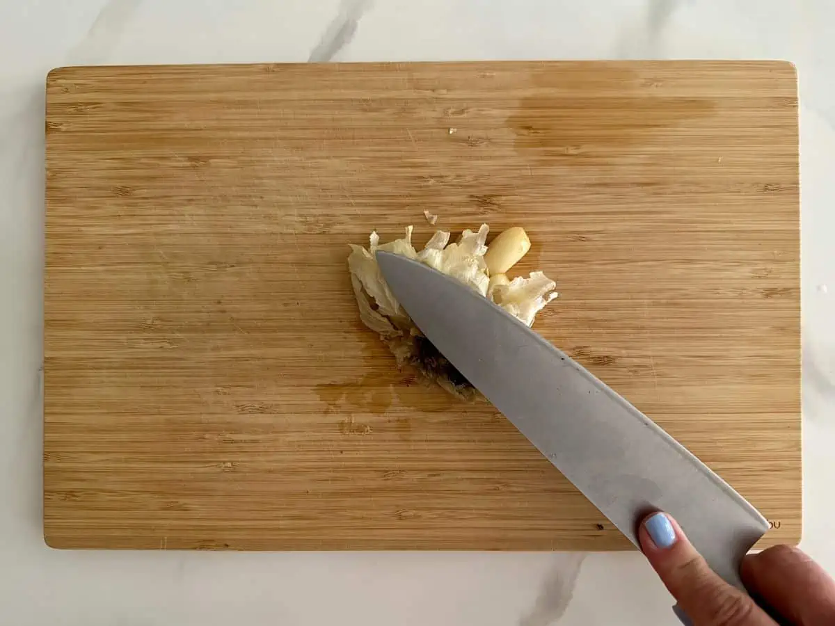 Using a knife to smash the cloves of roasted garlic.