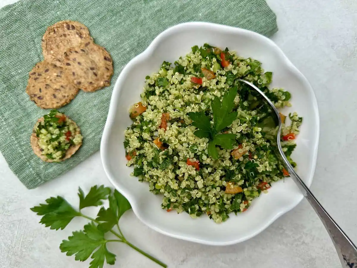 A plate of tabbouleh quinoa on the table with tomatoes in it and some crackers on the side.